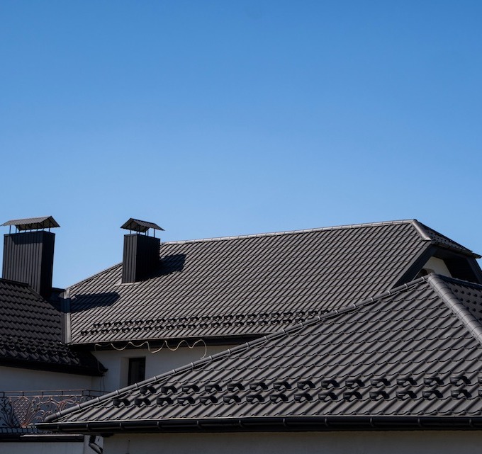 A brand new brown metal roof installation on a residential home. The roof is depicted with two chimneys.